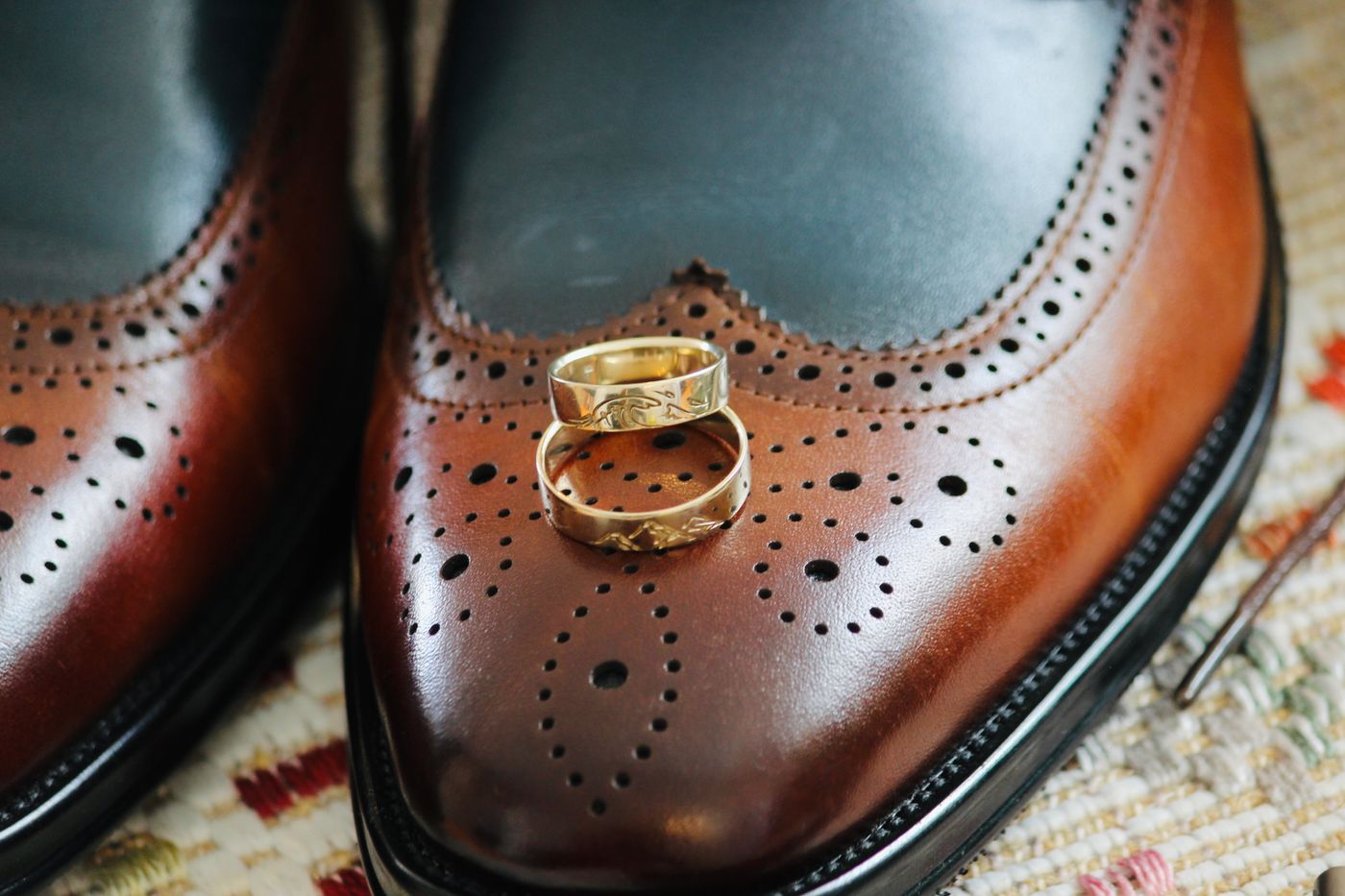 Two gold engagement rings resting on brown brogue shoes